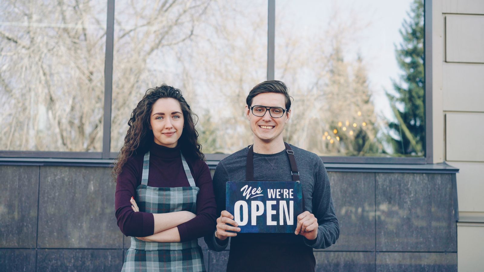 Two small business owners outside their shop holding an open sign
