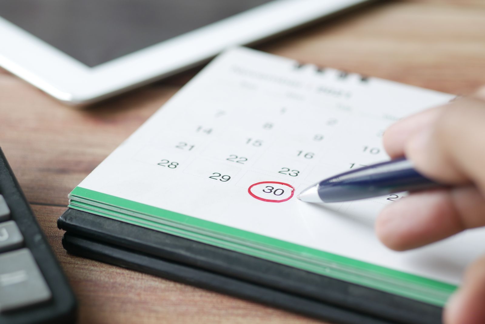 Hand circling a date on a calendar with a pen