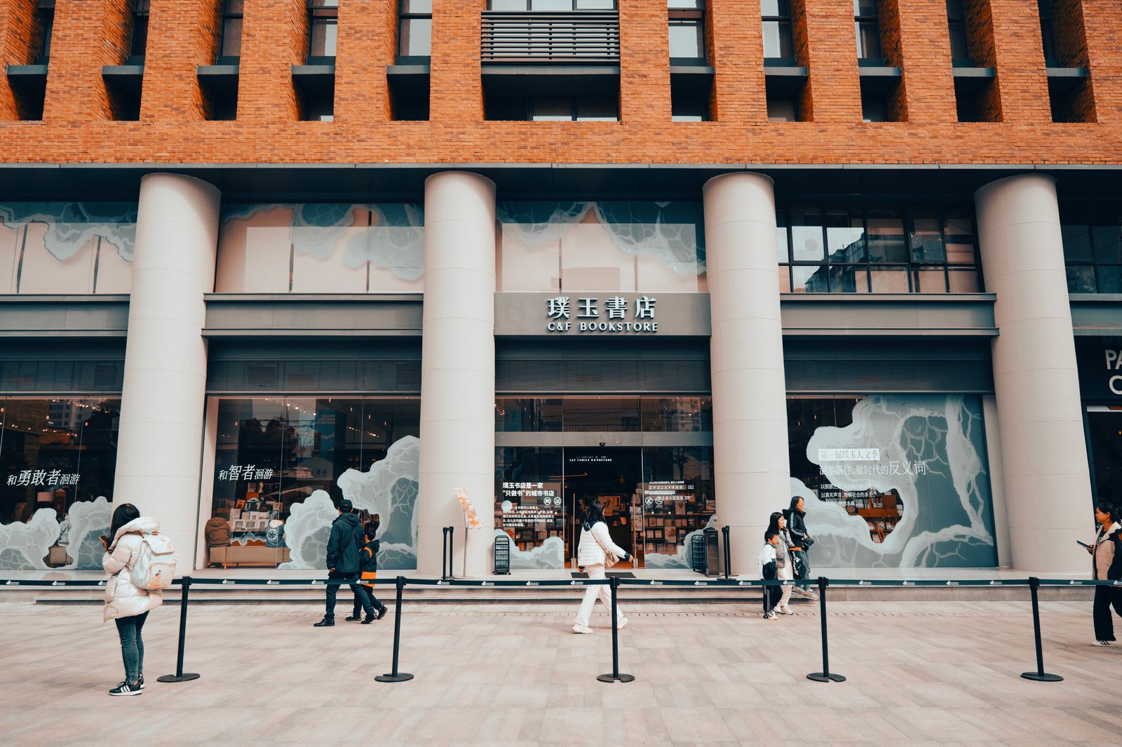People walking past a storefront with columns on a city street
