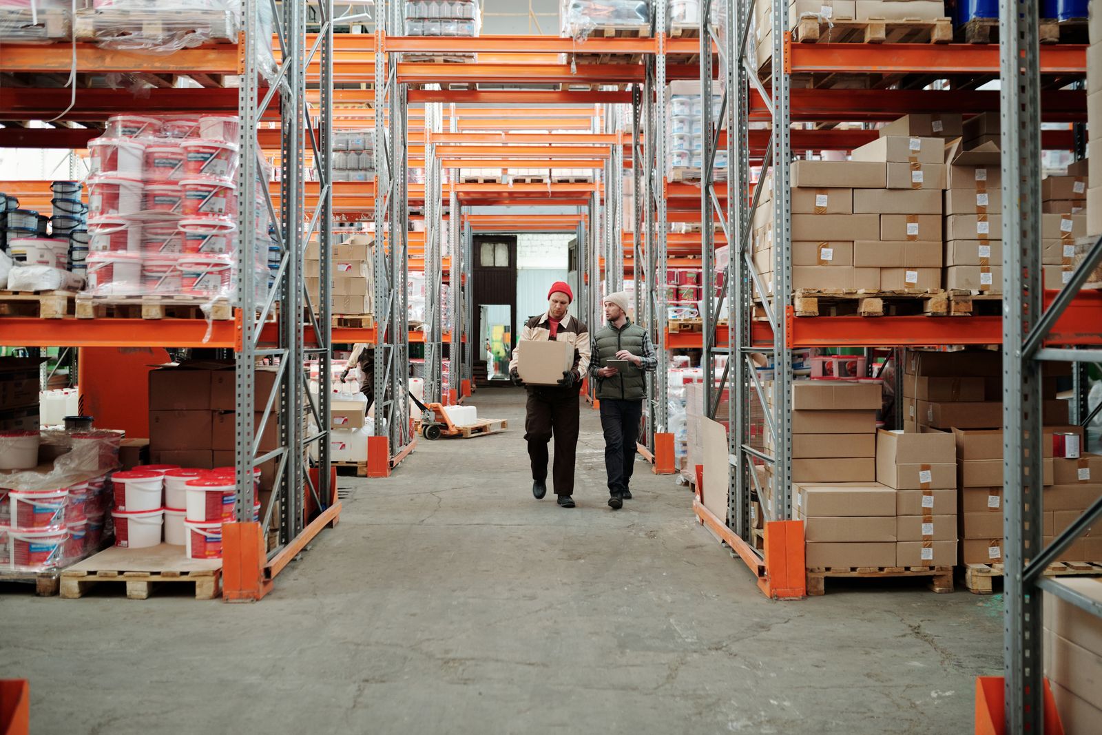 Two workers walking through a warehouse aisle lined with stocked shelves