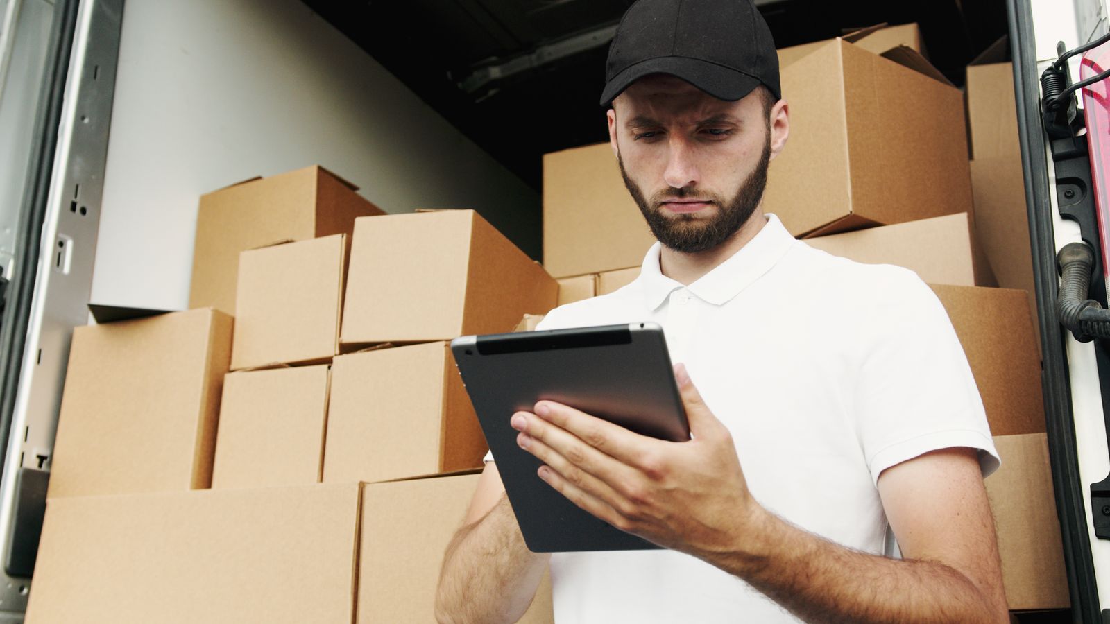 Delivery worker checking shipments on a tablet in front of stacked boxes