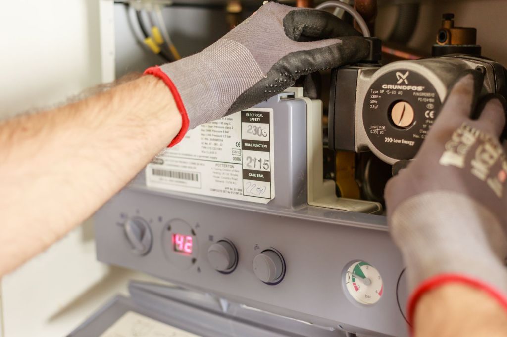 Gloved hands of a plumber adjusting a boiler during maintenance