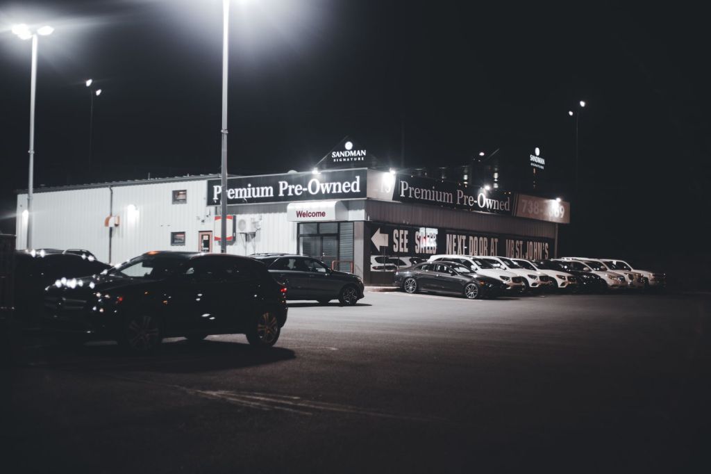 A lit dealership lot displaying pre-owned vehicles in the evening